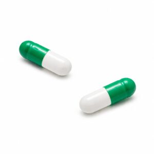 Zwei grün-weiße Kapseln mit der Aufschrift „THC-Kapseln 2,5 mg Novacana 65 T 10 Stück“ sind auf einem schlichten weißen Hintergrund abgebildet, voneinander beabstandet und in verschiedene Richtungen geneigt.