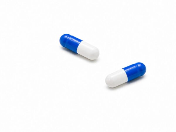 Zwei blau-weiße „Novacana THC Kapseln 2,5 mg“ mit einem Gehalt von jeweils 2,5 mg liegen auf einer schlichten weißen Fläche, im Abstand zueinander, ohne dass weitere Gegenstände im Bild zu sehen sind.
