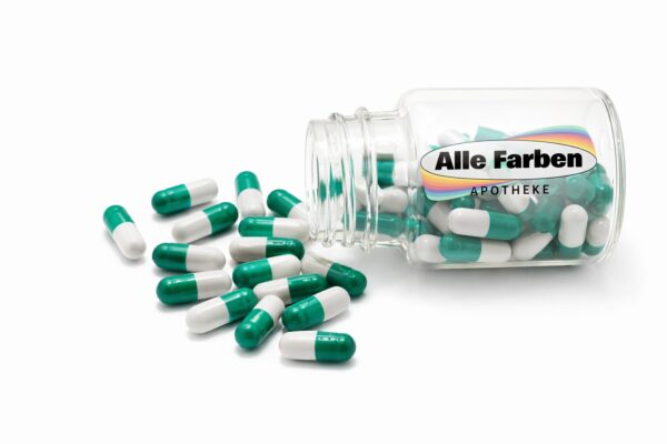 Ein Glasgefäß mit der Aufschrift Alle Farben Apotheke liegt auf der Seite und verschüttet grüne und weiße THC Kapseln 2,5 mg Novacana 65 T auf eine weiße Fläche. Einige Kapseln bleiben drinnen, während andere draußen verstreut sind.