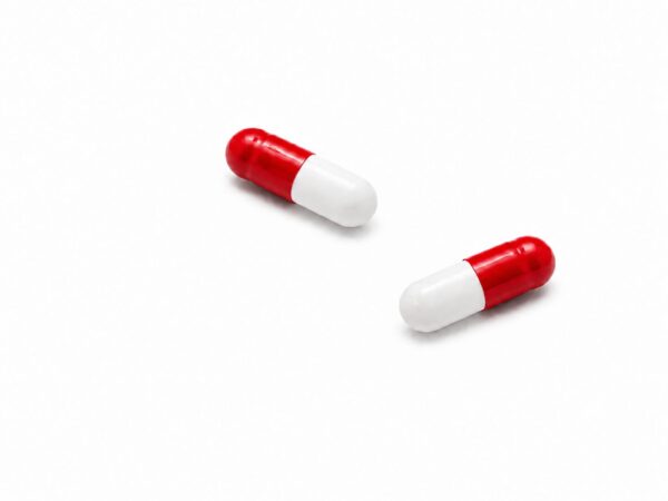 Zwei rot-weiße Kapseln der Sorte „THC Kapseln 20 mg Novacana“ aus der Packung „65 T 10 Stück“ sind vor einem schlichten weißen Hintergrund abgebildet.